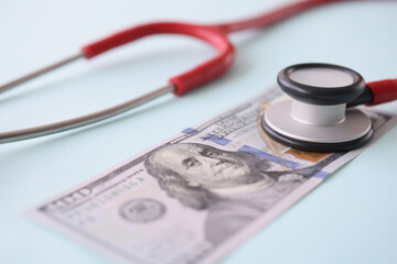 Red stethoscope lying on american dollar bill closeup