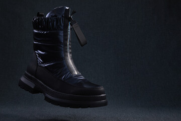 Fashion black unbranded boot flying on dark background. Black winter walking shoes levitate in air. Modern stylish female shoes for off-road walking.