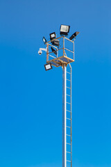 Pole with spotlights and CCTV camera at a ski resort. Against the background of the blue sky. Mountain slope lighting for snowboarding. Ski tours on a sunny day.