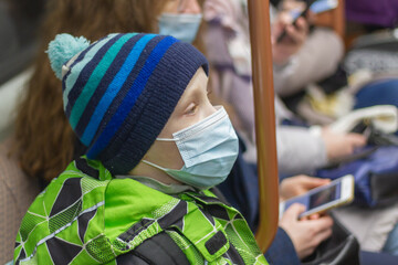 A child in a medical mask and hat rides in a subway car in spring, winter or autumn