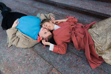 two bright lesbian girls lie on a stone staircase in the street, smiling. The concept of LGBT love. High quality photo