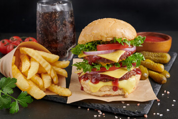 Homemade hamburger or burger with fresh vegetables and cheese lettuce and mayonnaise served, French fries on pieces of brown paper on black stone table . concept of fast food and junk food