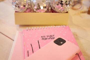 Pink notebook and wood table. Pink cell phone and Christmas ball