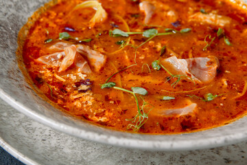 Russian cuisine - Solyanka Soup on dark textured table. Spicy and sour soup with meat slice and vegetables. Ceramic bowl on dark background.