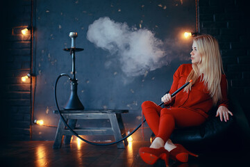 Fototapeta premium girl smokes hookah / beautiful glamorous girl in red dress smokes a hookah, the sexy model in a night club smokes