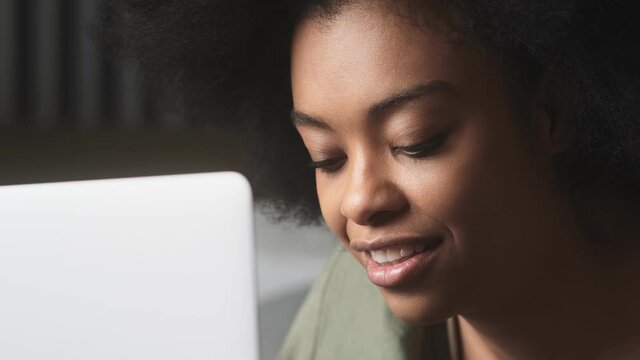 A close-up shot of a black smiling woman looking at a laptop in a light room