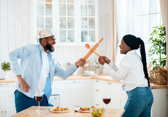 Funny Black Couple Having Fun In Kitchen, Using Kitchenware For Play Fight