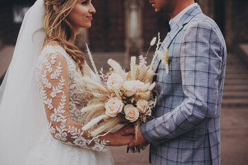 Amazing wedding couple. Pretty bride and stylish groom holding boho bouquet