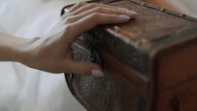 Close-up, caucasian female hand closes the lid of old leather chest with a latch in the room.