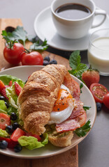 Delicious breakfast with fresh croissants, bacon sandwich with fried egg, tomato. milk served, coffee. strawberry, butterhead, blackberry salad. full american healthy breakfast top view.