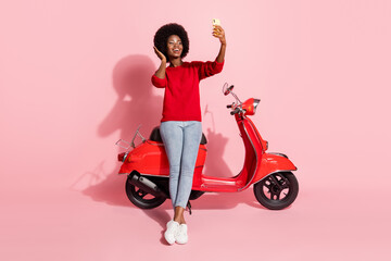 Fototapeta na wymiar Full body portrait of cheerful dark skin lady hand touch hair make selfie sit on moped isolated on pink color background