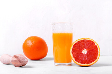 Blood orange juice freshly squeezed in the drinking glass with pulp and the fruits around on the white table
