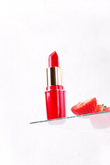 Red lipstick and strawberry on the glass showcase against the white background. Make-up product presentation