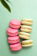 Pistachio and strawberry french  macaroon cookies on a light green background with copy space. Minimalistic sweet dessert composition.