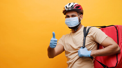 Studio shot of bicycle delivery man wearing protective face mask and blue protective gloves. Looking at camera and making thumbs up gesture.