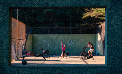 Three friends training outdoors,  seeing them through a window frame, woman upside down.