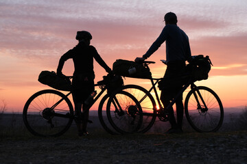 Bike packing cyclists leaning on their packed bikes during springtime sunset - 428808572