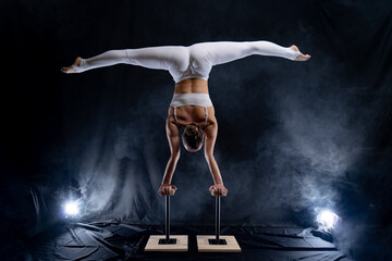 Flexible circus artist - female acrobat doing handstand on the back and smoker background © Hladchenko Viktor