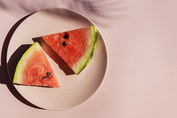 Fresh red watermelon slices on pink plate and tropical leaf shadow.