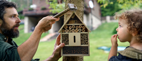 Small girl with father holding bug and insect hotel in garden, sustainable lifestyle.