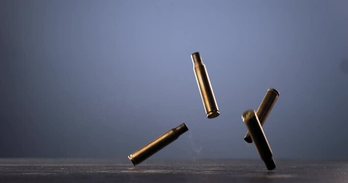 SUPER SLOW MOTION Empty machine gun shells falling on a ground against blue background. Shot with high speed camera at 420 FPS