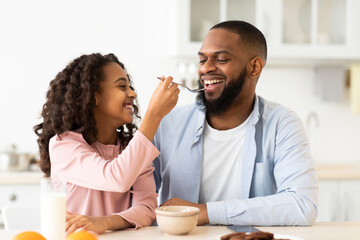Fototapeta na wymiar Cheerful african daughter feeding father with cereal