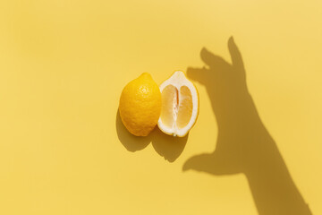 Two halved cuts of lemon with shadow from hand on yellow background