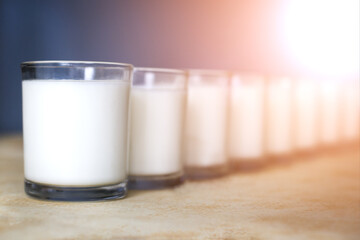 Fresh white cow or goat milk or ktfir stands on the table in the rays of the gentle yellow sun, blurred background, selective focus,containers with sour cream stand on the table in transparent glasses