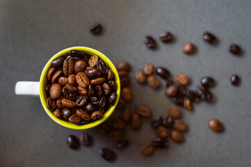 Cup of coffee with roasted coffee beans inside of different shades and kinds on a gray background. Coffee beans surrounding mug. Copy space