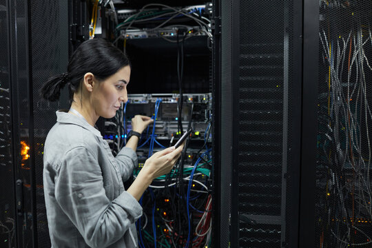 Side view portrait of female network technician connecting cables in server cabinet while setting up supercomputer at data center, copy space