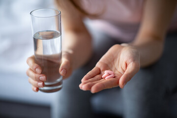 Antiviral therapy. Cropped view of millennial lady with glass of water taking tablets to treat coronavirus at home