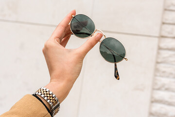 A woman's hand holds a pair of sunglasses. Outdoor close-up