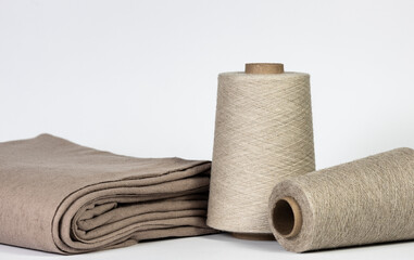 A spool of linen thread near a neatly folded linen cloth. Sewing workshop of a tailor shop. Flat lay on white background, copy space.