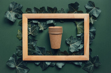 Eco friendly craft paper cups on green background with wooden frame and ivy leaves. Recycling and...