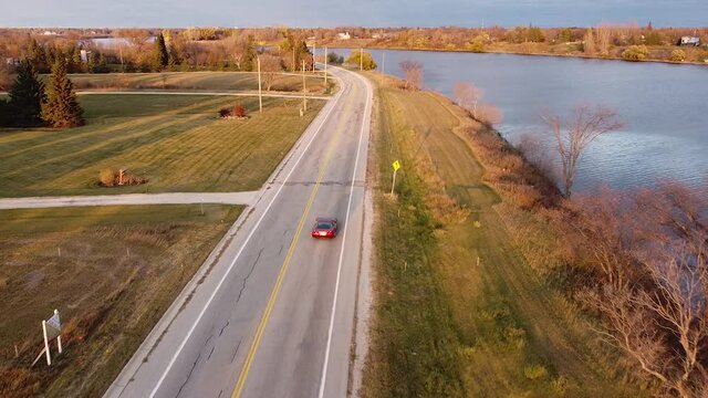 Red Corvette Driving Down Fall Riverside Road