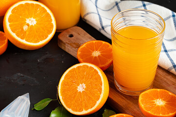 Glass of orange juice and cut oranges on table