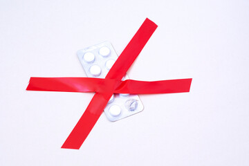 Red cross made of two pieces of insulating tape and pill packaging on white background