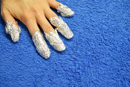 Removing shellac from nails. fingers with foil on blue background. Close-up hand
