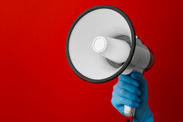 Human hand in medical glove holding electronic megaphone on red background