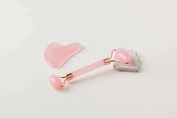 Rose quartz gua sha stone, jade roller on a light background. The concept of home skin care. Copy space.