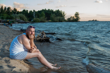 Funny bald man with red beard dressed in underwear posing on the beach. A humorous male parody of a glamorous girl.