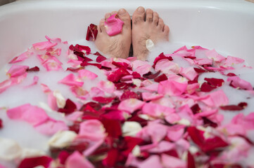 Funny picture of a man taking a relaxing bath. Close-up of male feet in a bath with foam and rose petals