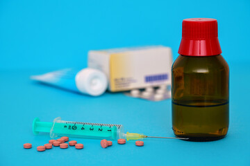 Syringe, pills and medicine bottle. Various medications are in the background.