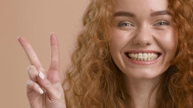 Red-Haired Millennial Woman Gesturing Victory Sign Posing On Beige Background