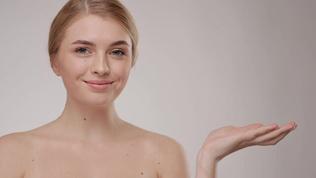 Slow Motion. On grey background. Close up. Beautiful young caucasian blonde woman with grey eyes and smooth healthy skin holding a hand. White Cream Skin Care Cosmetic Concept.