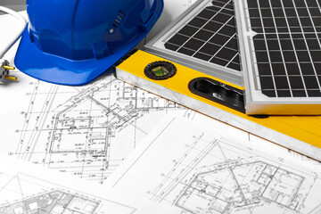 Construction blueprints, hardhat and solar battery on architect's table