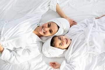 Happy mother and daughter in bathrobes laying on bed
