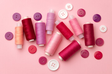 Fototapeta na wymiar Multicolored thread spools and buttons on pink background