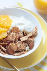 Whole grain oats and wheat flakes with orange, almond nuts and yogurt in a white bowl. Healthy morning breakfast concept close up