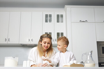 Happy mom and baby cook in a white kitchen at a table made of dough, they are very good and fun together